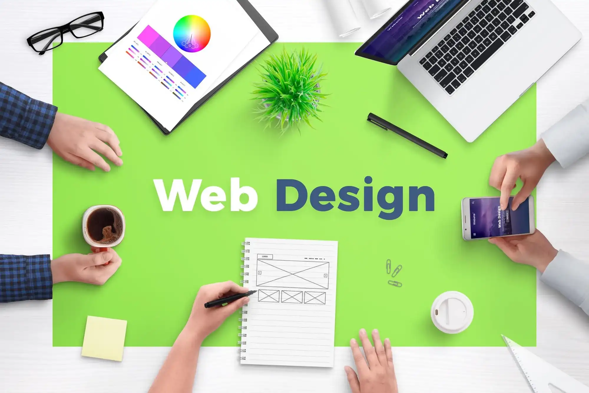 Hands working on web design elements on a green desk. Includes a laptop, coffee, phone, notepad, and color chart. Text: Web Design.