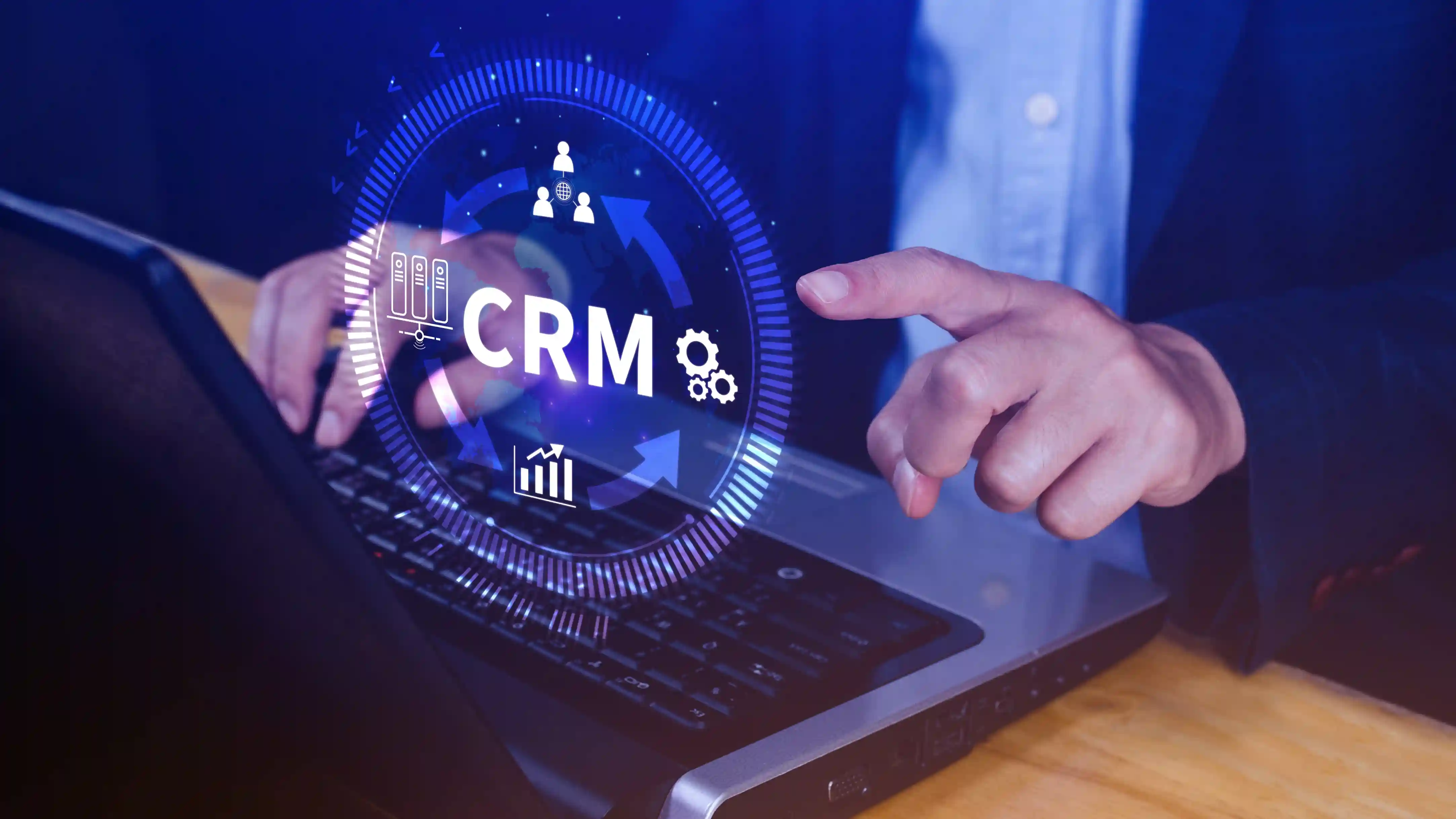 Person points at a glowing CRM hologram above a laptop. Blue tones dominate, reflecting modern tech and business themes.